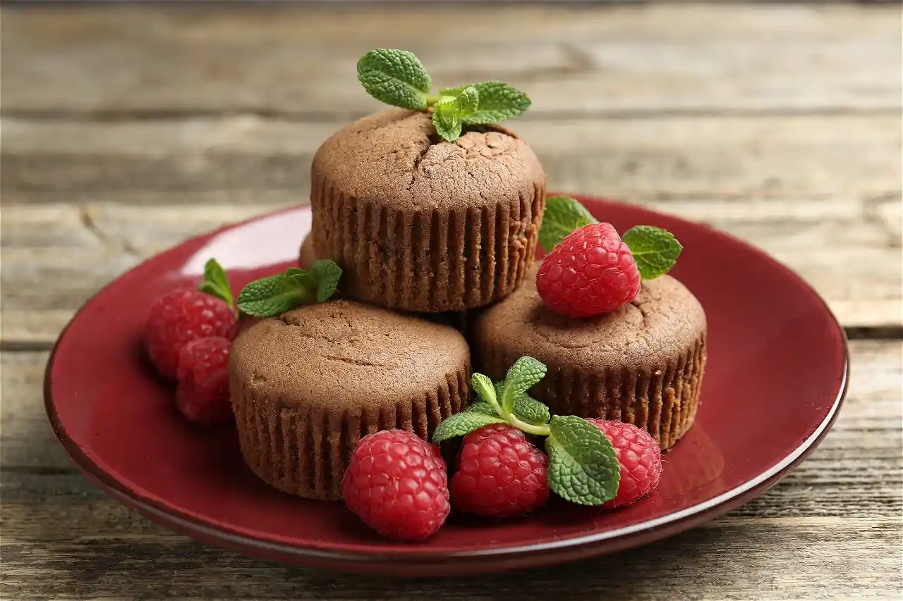 Schokoladenmuffins auf einem Teller mit frischen Himbeeren und Minzblättern